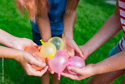  Cropped image of girls holding water balloons in hands. Joint games with water for kids. Summer fun outdoor activities for children concept.