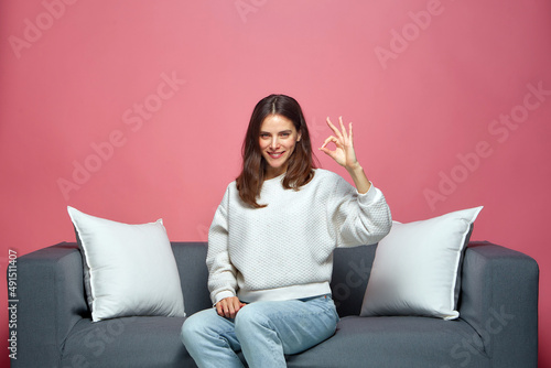 Smiling satisfied young girl showing ok gesture sign recommend product or service, sitting on sofa. Positive feedback