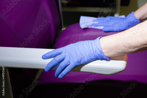 hand with a glove and a blue cloth cleaning a purple chair in a hospital