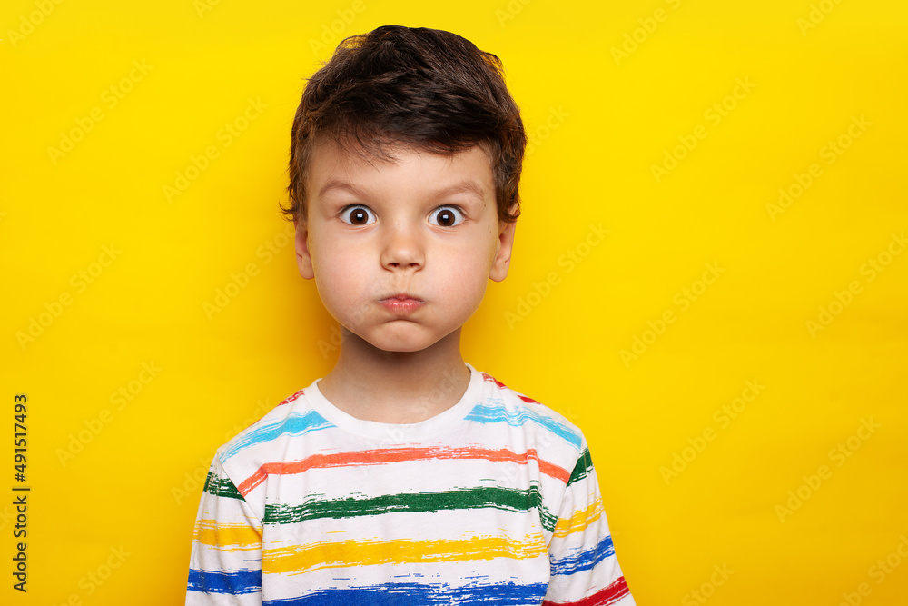 Handsome caucasian child wearing casual white T-shirt with bright stripes puffing cheeks with funny face. mouth inflated with air, crazy expression. - obrazy, fototapety, plakaty 