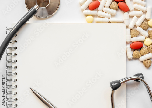 White blank page in notebook on white background with stethoscope and group of pill. Medical concept. Term and abbreviation. Place for writing
