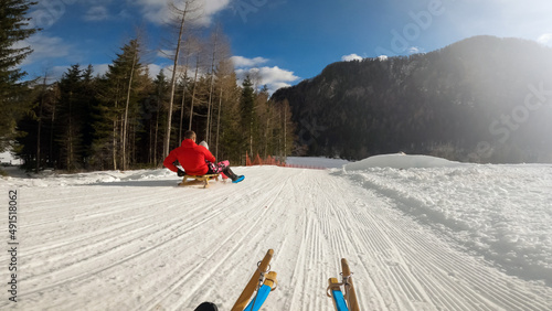 Point of view of a child sledding with father and sister, riding a wood sled on the hill on sunny clear winter day. photo