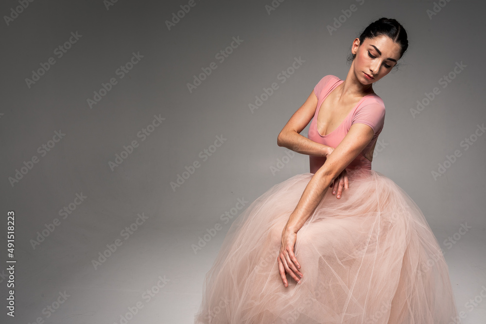 Fototapeta premium young pretty, fragile, beautiful ballerina dancing in a long pale pink dress with a tulle on a uniform background, hand movements, restrained tone. Ballet, dance, dancer. Place for inscription
