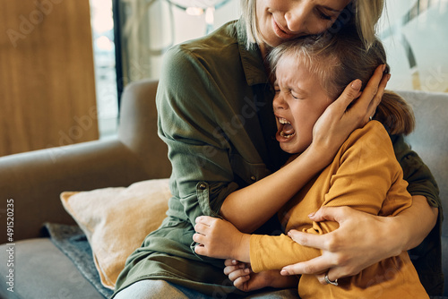 Upset little girl crying while caring mother is consoling her.