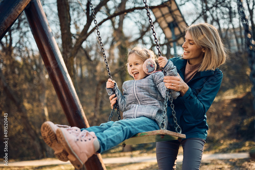 Carefree girl has fun while mother is pushing her on swing on playground in nature. © Drazen