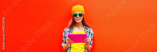 Portrait of stylish cool young woman model with tablet pc wearing colorful clothes on vivid background, blank copy space for advertising text