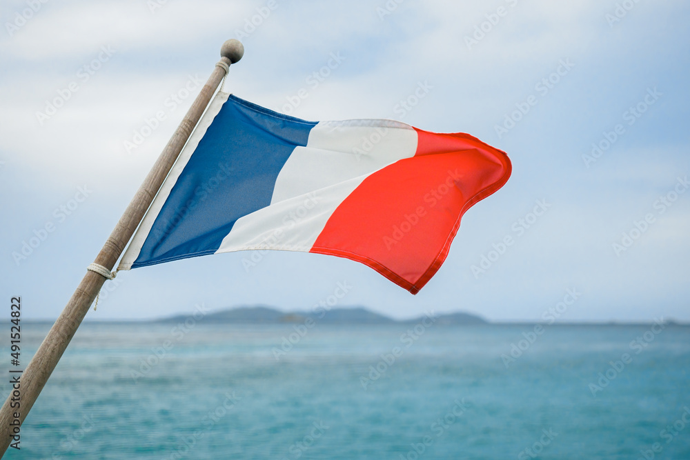 The French tricolor flag flies on the back of the yacht, against the backdrop of the coastal landscape. The concept of yachting, sea travel