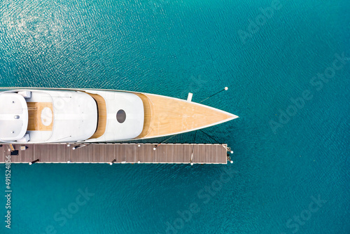Aerial view of a luxurious white modern expensive yacht moored to a long pier in a bay with crystal clear turquoise ocean water. Close-up. Tourism concept