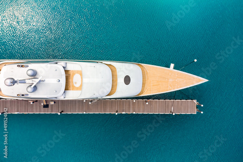 Aerial view of a luxurious white modern expensive yacht moored to a long pier in a bay with crystal clear turquoise ocean water. Close-up. Tourism concept © Sergey Chips