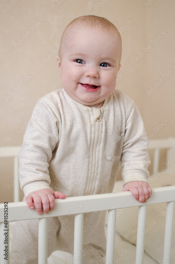 Portrait of a little smiling infant baby girl standing in a crib in the bedroom of the house. Teeth cut, salivation concept Portrait of a little smiling infant baby girl standing in a crib in the bedroom of the house. Teeth cut, salivation concept