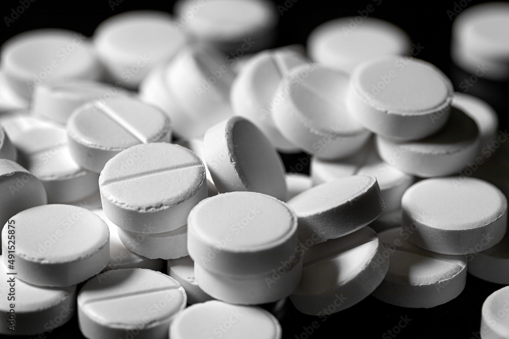 Close up of white painkiller tablet on a reflective black background Close up of white painkiller tablet on a reflective black background