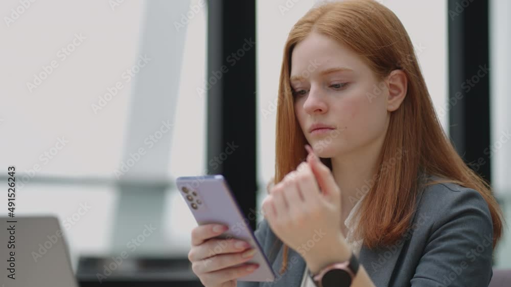 Beautiful young business woman using phone in office. Woman using a smartphone and leaning on a window texting sending emails planning meetings networking online browsing messages on mobile phone Beautiful young business woman using phone in office. Woman using a smartphone and leaning on a window texting sending emails planning meetings networking online browsing messages on mobile phone