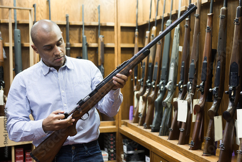 Portrait of ordinary confident man in gun shop showing rifle