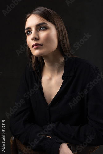 Portrait of a young brunette with long hair in the studio. Dramatic photo in dark colors.