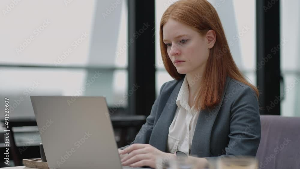 A young red-haired woman is working on a laptop. Remote work. Home office. Office work. A woman in a suit in the office is typing on a laptop A young red-haired woman is working on a laptop. Remote work. Home office. Office work. A woman in a suit in the office is typing on a laptop