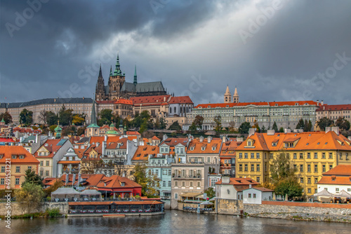 View of Prague in Czech Republic from Charles Bridge featuring Prague Castle, apartment buildings, shops and water, daytime, dark sky, nobody