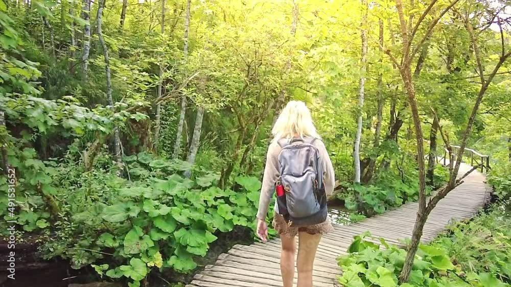 SLOW MOTION: girl backpacker walking on the jetty bridge of Plitvice Lakes National Park in Croatia in the Lika region. UNESCO World Heritage of Croatia named Plitvicka Jezera.