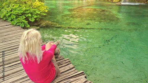 Woman backpacker sitting on the wooden jetty under the waterfall of Milino Jezero lake. Plitvice Lakes National Park in Croatia in the Lika region. SLOW MOTION. photo