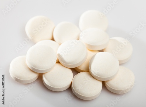 Closeup view of heap of identical round pills on white surface..