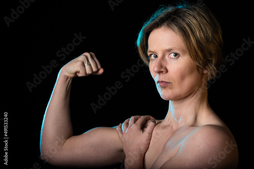 Low key studio portrait of a 35 year old white woman with naked shoulders showing her biceps