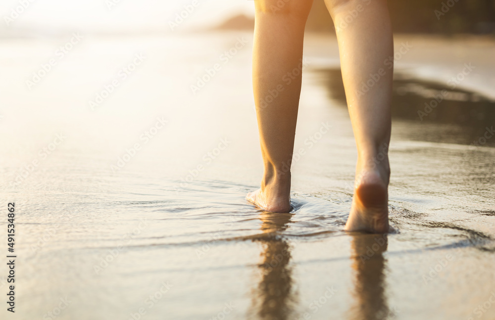 Close up woman feet walking on the beach with the sunset. Travel in holiday summertime. Female standing on the sand at the beach with sea water in the evening. Relaxing Vacation time Close up woman feet walking on the beach with the sunset. Travel in holiday summertime. Female standing on the sand at the beach with sea water in the evening. Relaxing Vacation time
