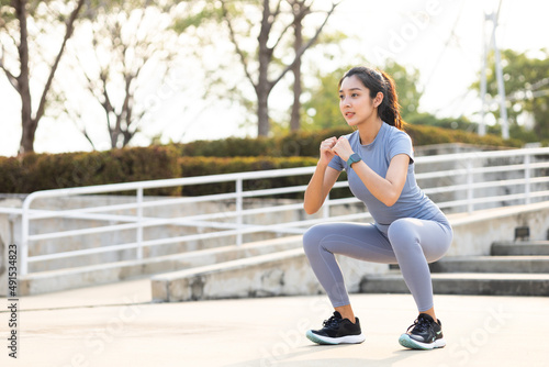 Beautiful fitness asian woman doing squat sit up exercise workout at sport stadium. Attractive female warming up body training wearing sportswear. Healthy and active lifestyle concept.