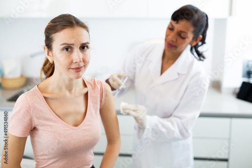 Hispanic woman doctor vaccinating young caucasian woman patient.
