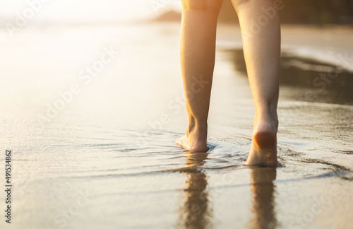 Close up woman feet walking on the beach with the sunset. Travel in holiday summertime. Female standing on the sand at the beach with sea water in the evening. Relaxing Vacation time