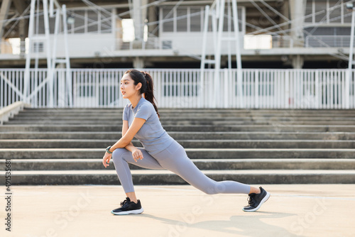 Healthy and fit asian woman wearing sportswear warming up in the city at sunrise. Confident young female stretching leg outdoor. before Workout exercise in the morning. Healthy lifestyle concept.
