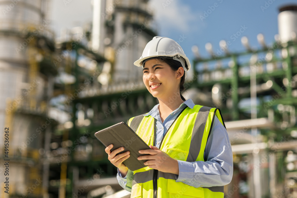 Asian engineer manager woman with white safety helmet standing front of oil refinery. Industry zone gas petrochemical. Factory oil storage tank and pipeline. Workers in the refinery construction. Asian engineer manager woman with white safety helmet standing front of oil refinery. Industry zone gas petrochemical. Factory oil storage tank and pipeline. Workers in the refinery construction.