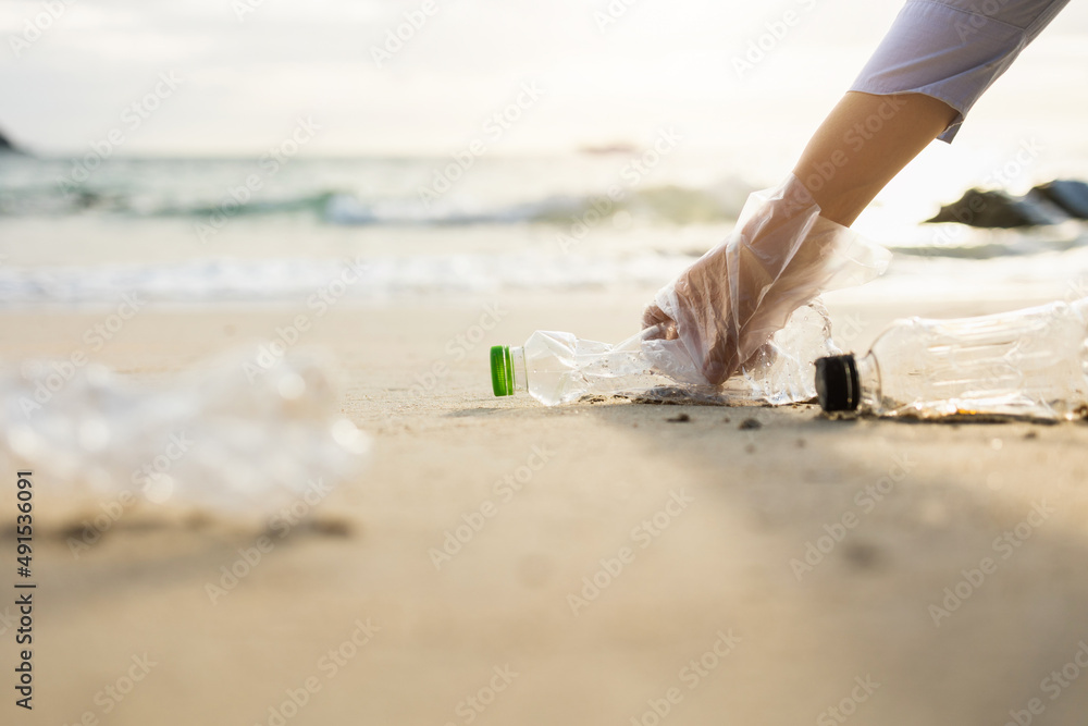 Close up woman hand pick up the plastic bottle on the beach. Female Volunteer clean the trash on the beach make the sea beautiful. World environment day concept.