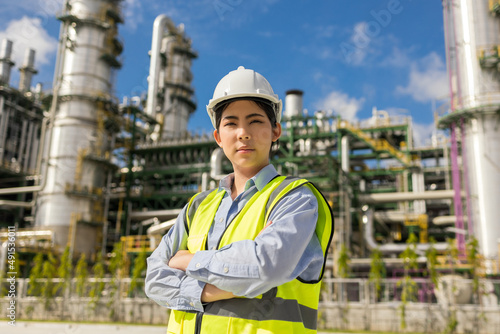 Asian engineer manager woman with white safety helmet standing front of oil refinery. Industry zone gas petrochemical. Factory oil storage tank and pipeline. Workers in the refinery construction. © Chanakon