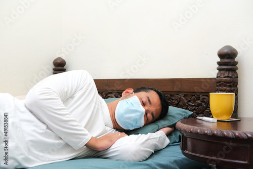 Adult Asian wearing medical mask when got sick and sleeping in his bed photo