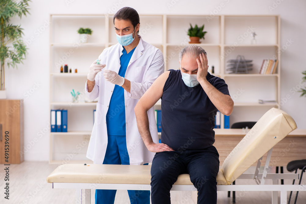 Fototapeta premium Old man visiting young doctor in covid-19 vaccination concept