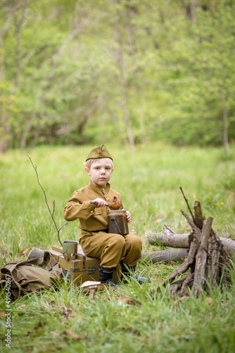 a small child in a beautiful military victory uniform  playing in nature and eating soldier porridge