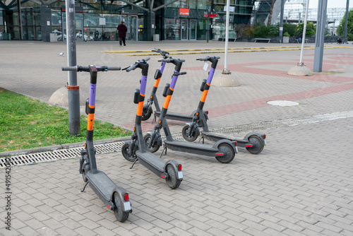 Three electric scooters stand at the edge of the sidewalk.