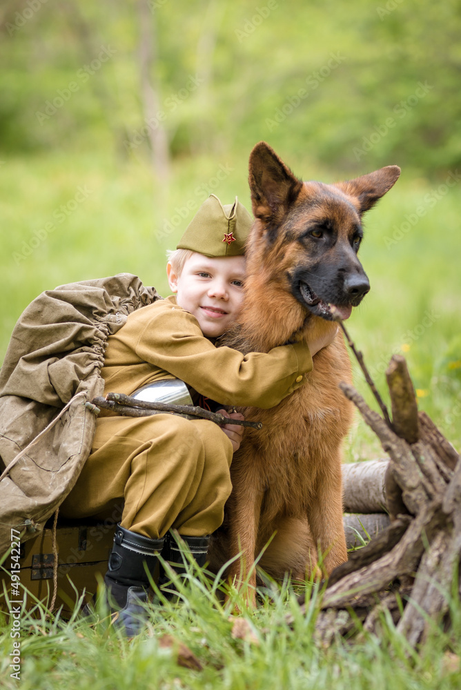 a boy in a military uniform in a clearing, sitting by a campfire with a German shepherd.Two friends defend the motherland a boy in a military uniform in a clearing, sitting by a campfire with a German shepherd.Two friends defend the motherland