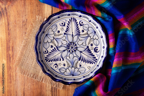 Mexican Cuisine Background, colorful traditional fabric and empty talavera style plate on wooden rustic table. Flat lay photo