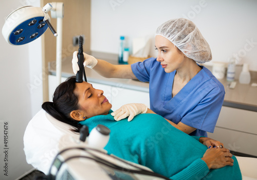 Latino american woman receiving face ultrasound lifting procedure in clinic of aesthetic cosmetology
