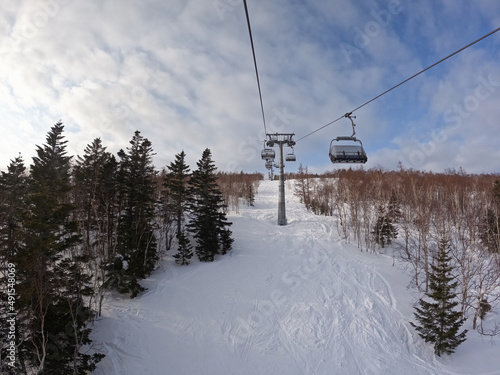 A cable car that transports skiers and snowboarders on a winter slope. On a sunny winter day in a ski resort, the lift goes up, carries people, top view from a chair lift on a snowy background.