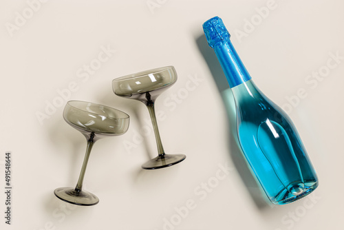 Champagne glasses tinted grey glass, Blue Champagne or blue sparkling wine bottle. Light Festive drink concept, glare and sunlight. Modern wine colored glasses. Creative flat lay