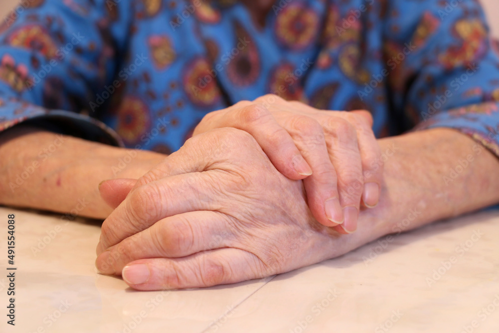 Symptoms of arthritis disease. Close-up of a tremor (shaking) of the hands of a middle-aged female patient on a white table. The concept of mental health and neurological disorders. Symptoms of arthritis disease. Close-up of a tremor (shaking) of the hands of a middle-aged female patient on a white table. The concept of mental health and neurological disorders.