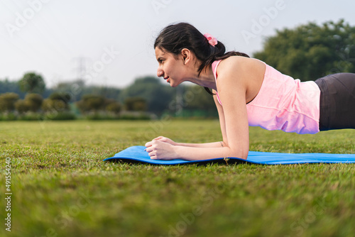 Young indian girl doing planks in the park. Girl stretching and doing yoga in yoga mat. Healthy lifestyle concept.