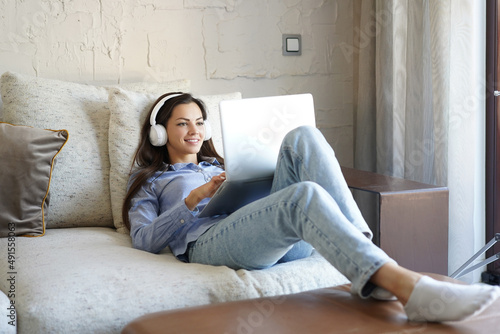 Pretty girl using laptop on couch at home in the living room. Listening music, relaxation after a hard week.