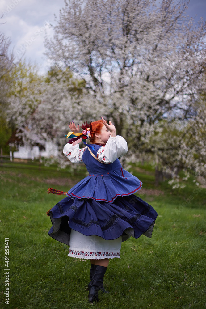 Young woman in national Ukrainian costume. Smiling Young Lady in traditional Clothes dancing near blooming tree. Peace in Ukraine