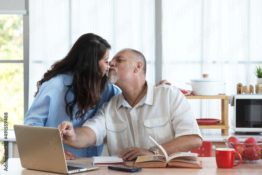 Asian middle-aged woman kisses her caucasian husband, man working from home, Valentine's day Asian middle-aged woman kisses her caucasian husband, man working from home, Valentine's day