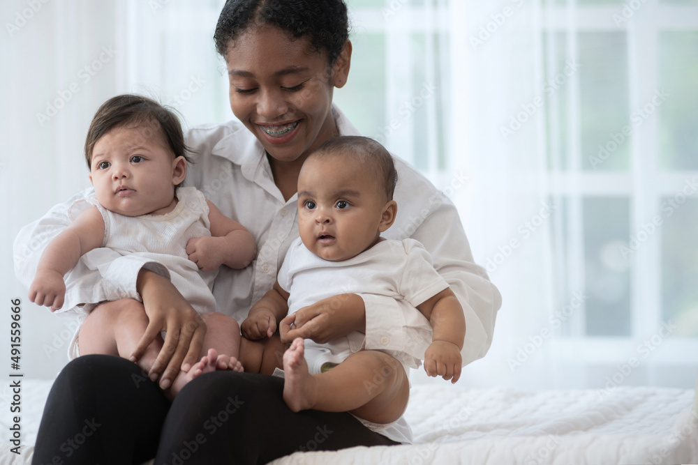 Happy young dark skinned woman with different skin color baby, in her arm on bed, smiling and hugging, different skin color Happy young dark skinned woman with different skin color baby, in her arm on bed, smiling and hugging, different skin color