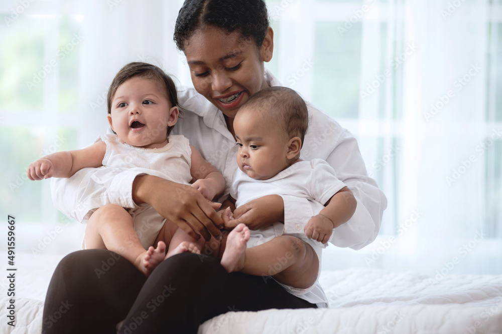 Happy young dark skinned woman with different skin color baby, in her arm on bed, smiling and hugging, different skin color Happy young dark skinned woman with different skin color baby, in her arm on bed, smiling and hugging, different skin color