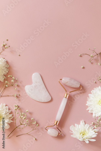 Rose quartz facial massage roller over pink background with gypsophila flowers. Massage tools with jade stone, anti-aging, anti-wrinkle beauty skincare tool. Top view flat lay. Copy space. photo