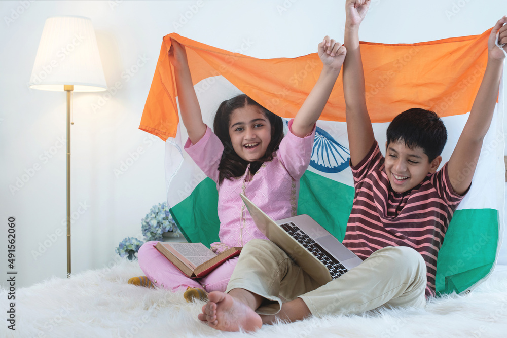 Indian brothers and sisters with laptops on lap sitting on bed, holding